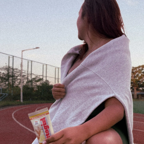 Confident female athlete on track field holding Attagirl protein bar made for performance